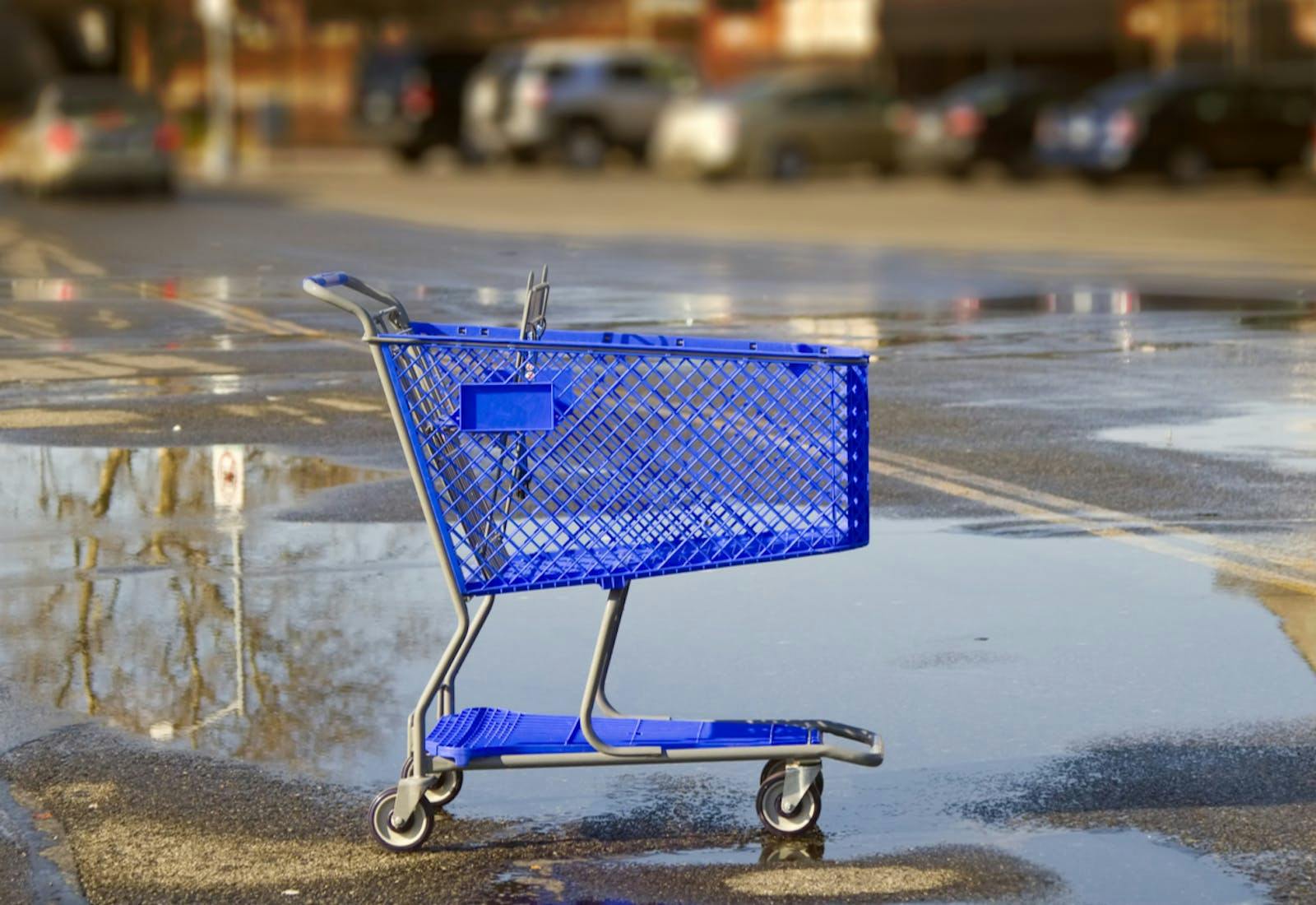 An empty shopping cart stands in a rainy parking lot